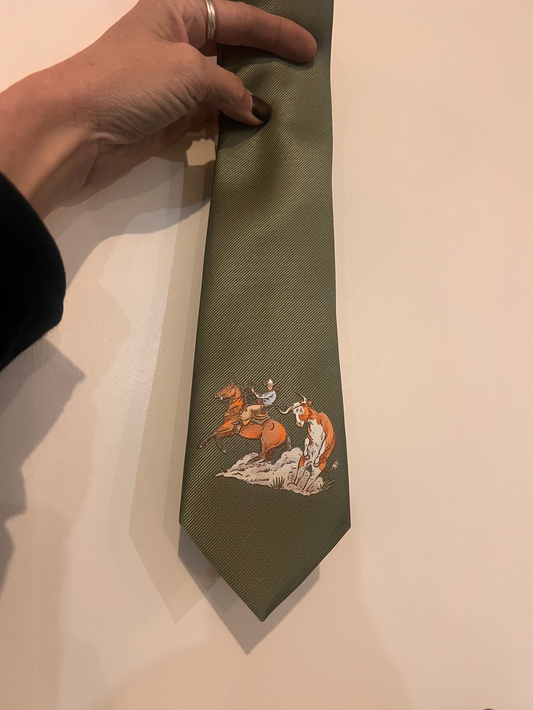Green tie with embroidered design held by a hand on a beige background