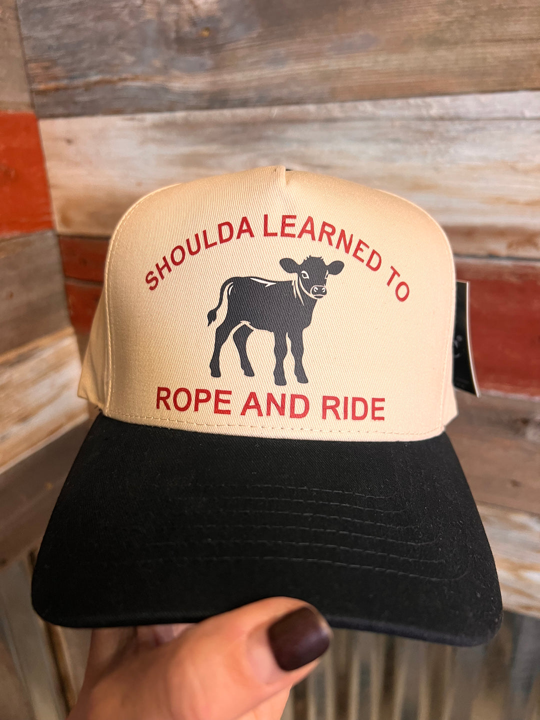 Cap with text and graphic held by a hand against a wooden background