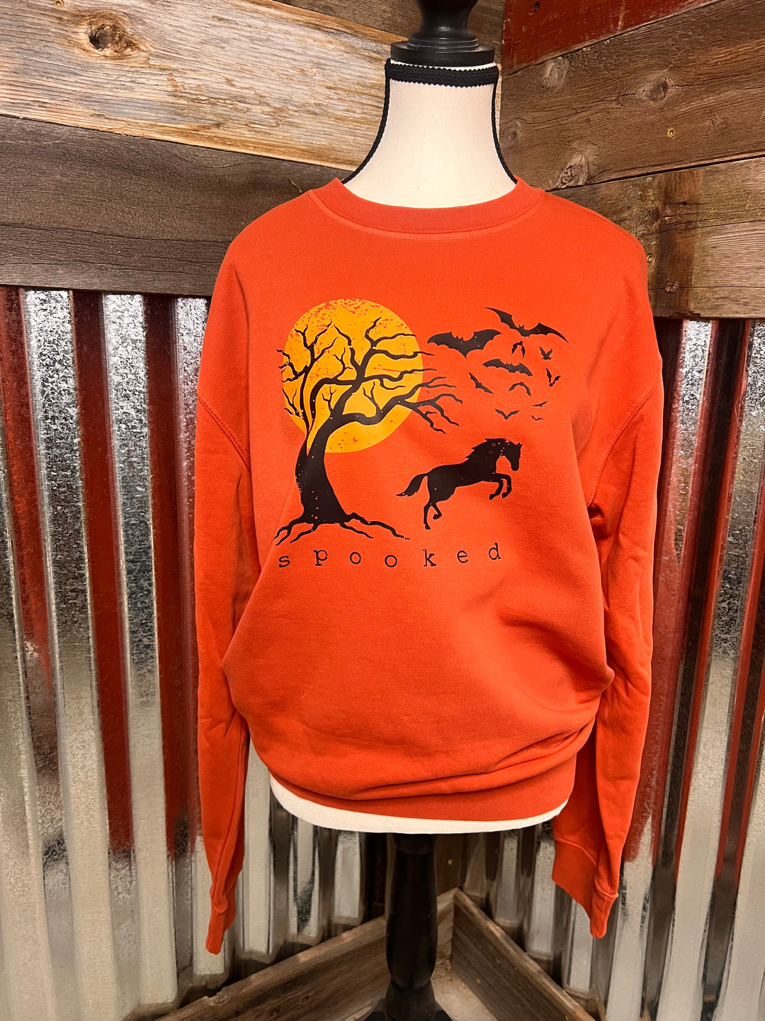 Orange sweater with a black tree and moon design on a wooden surface