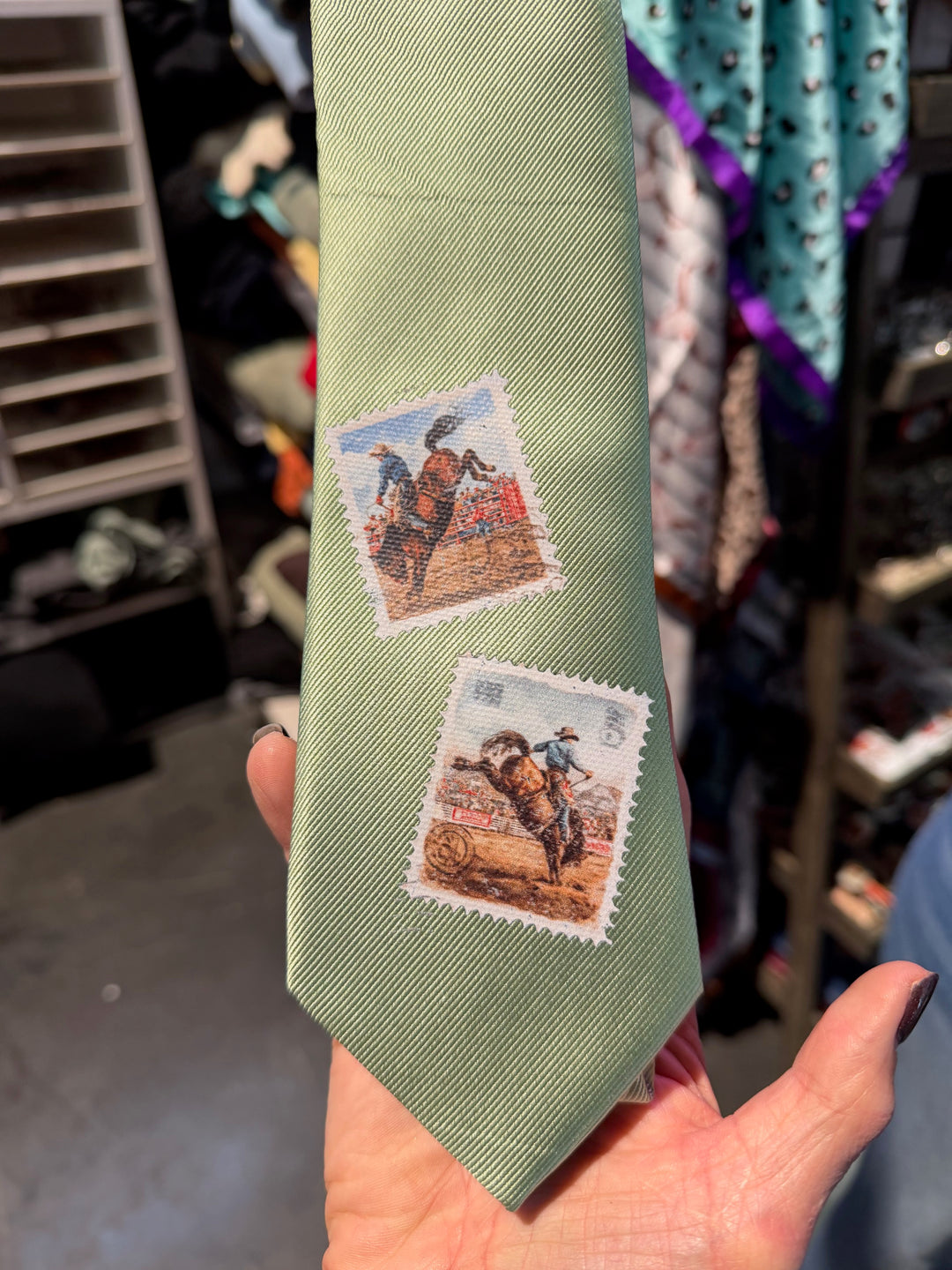 Green tie with vintage stamp designs held by a hand in a store setting