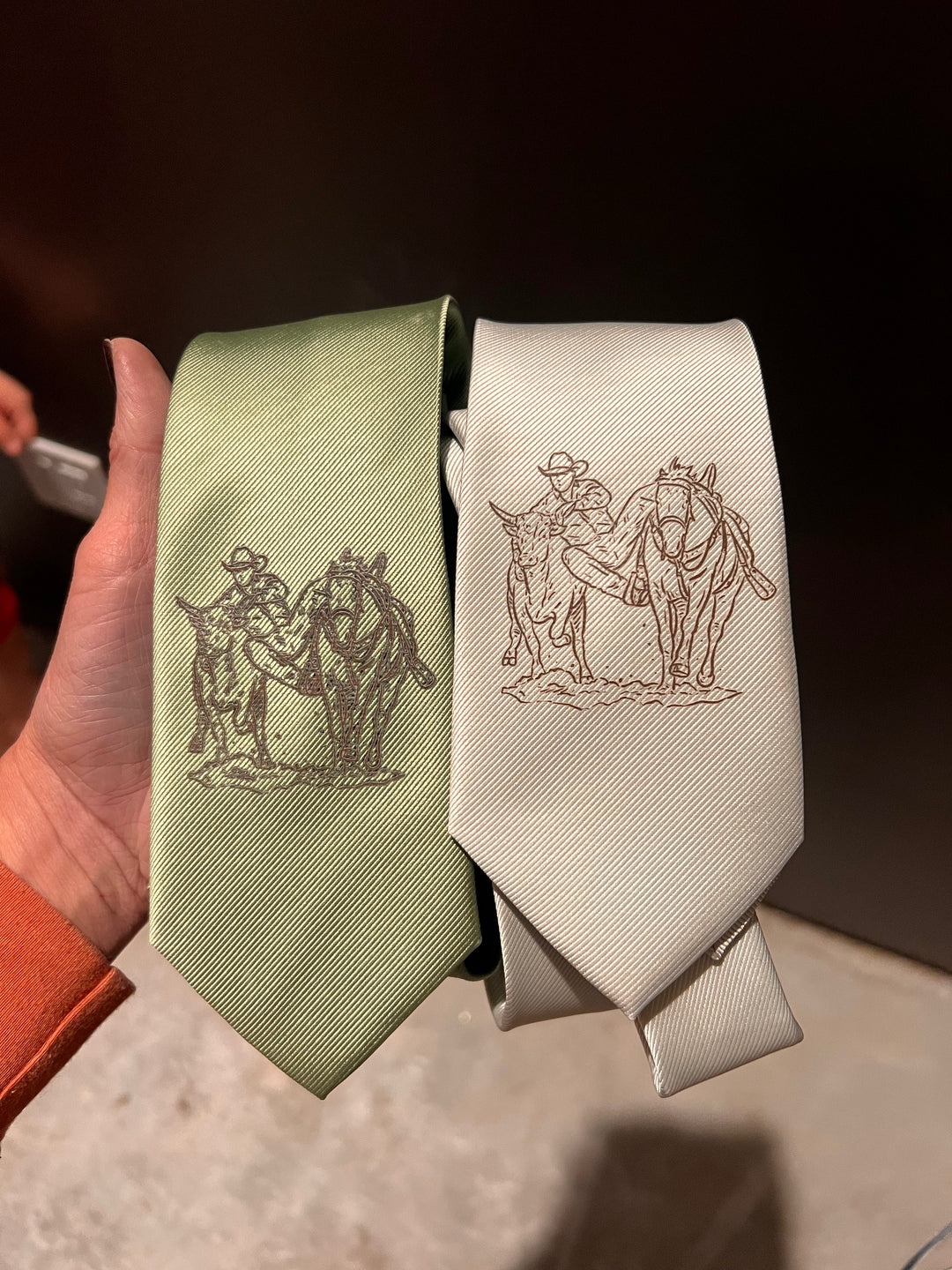 Two ribbons with embroidered designs held by a hand against a dark background