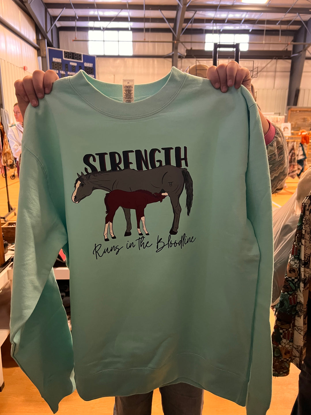 Person holding a light green t-shirt with a graphic design and text.