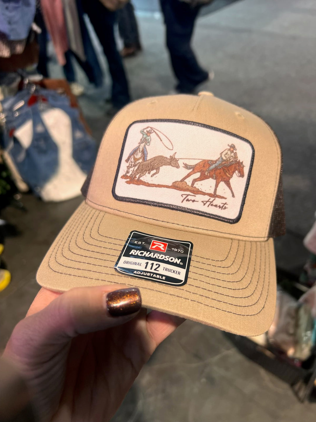 Beige cap with a logo and text held by a hand against a blurred background