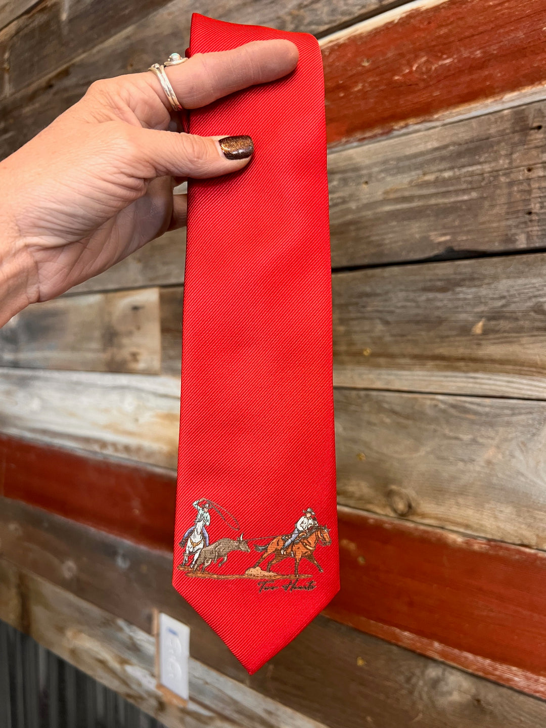 Red tie with a design held by a hand against a wooden background