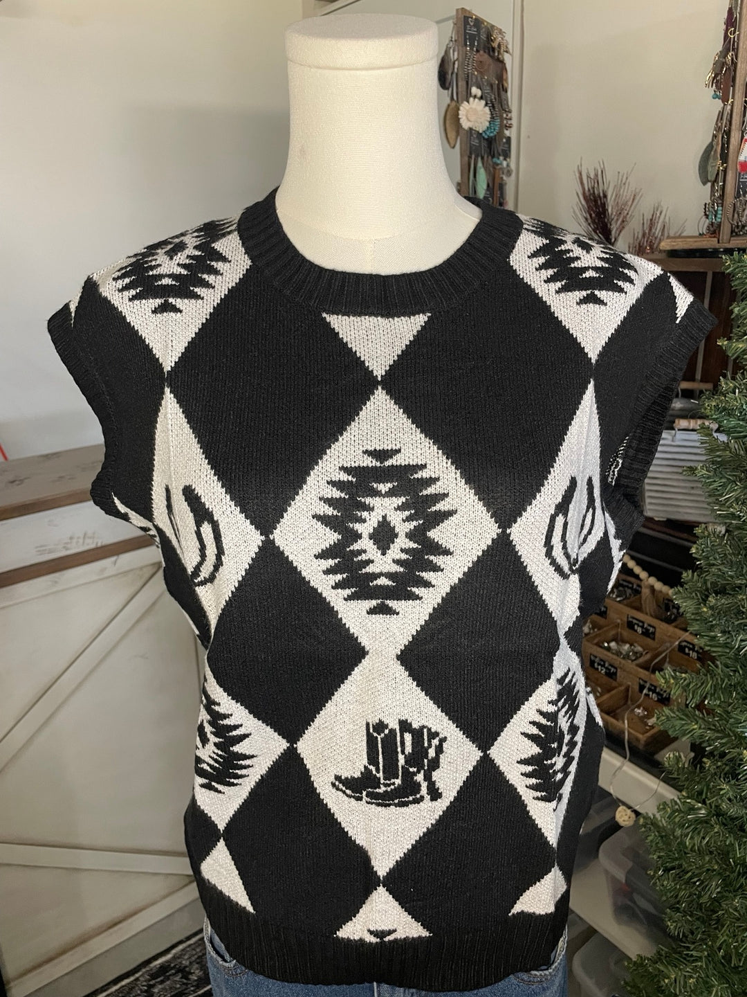A black and white argyle sweater vest with southwestern geometric patterns and a small boot graphic, displayed on a mannequin torso.