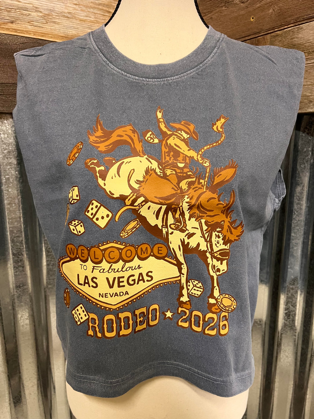 A sleeveless gray cropped T-shirt displayed on a mannequin torso, featuring a large front graphic of a cowboy riding a bucking horse with the text 'Welcome to Fabulous Las Vegas Nevada Rodeo 2026' in tan and orange tones.