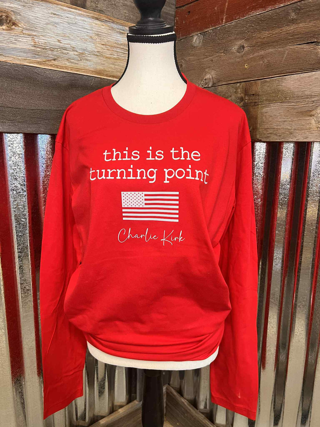 Red long-sleeve shirt with text and American flag on a mannequin against a wooden background