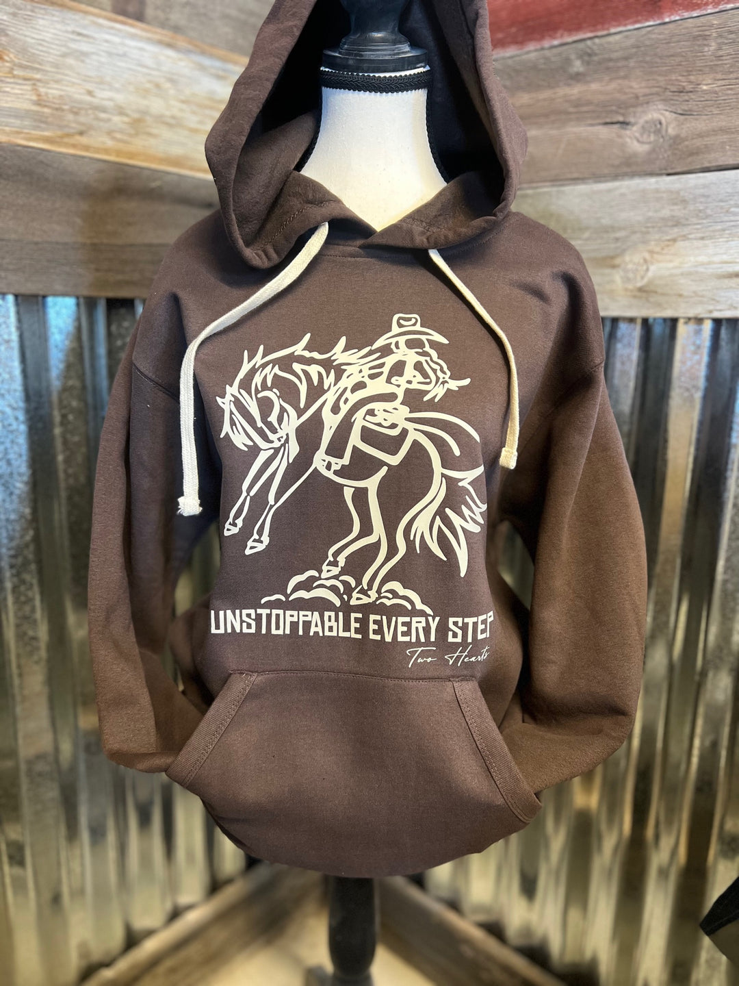 Brown hoodie with graphic design on a mannequin against a wooden background