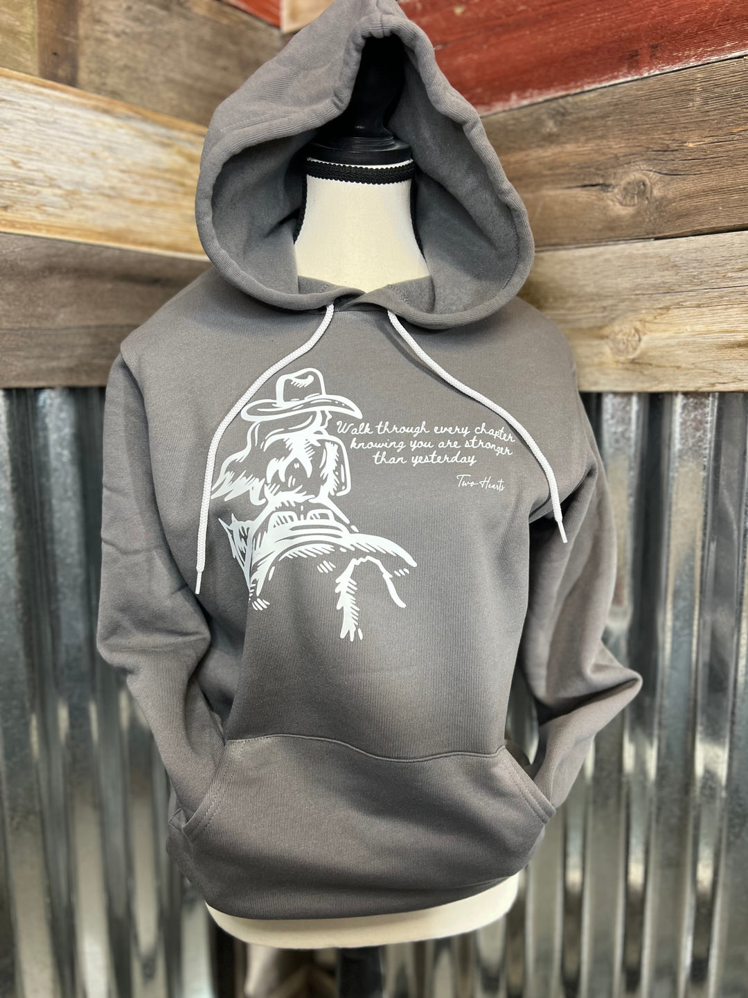 Gray hoodie with white graphic design on a mannequin against a rustic wooden and metal background
