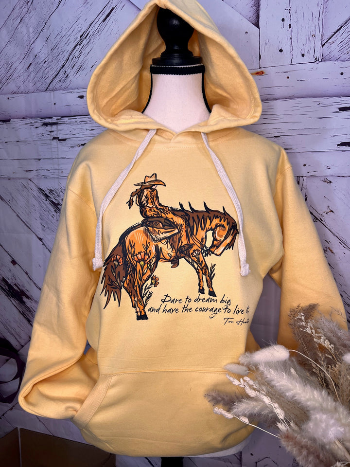 A person wearing a yellow hoodie with a graphic of a cowgirl riding a bucking horse and the text &