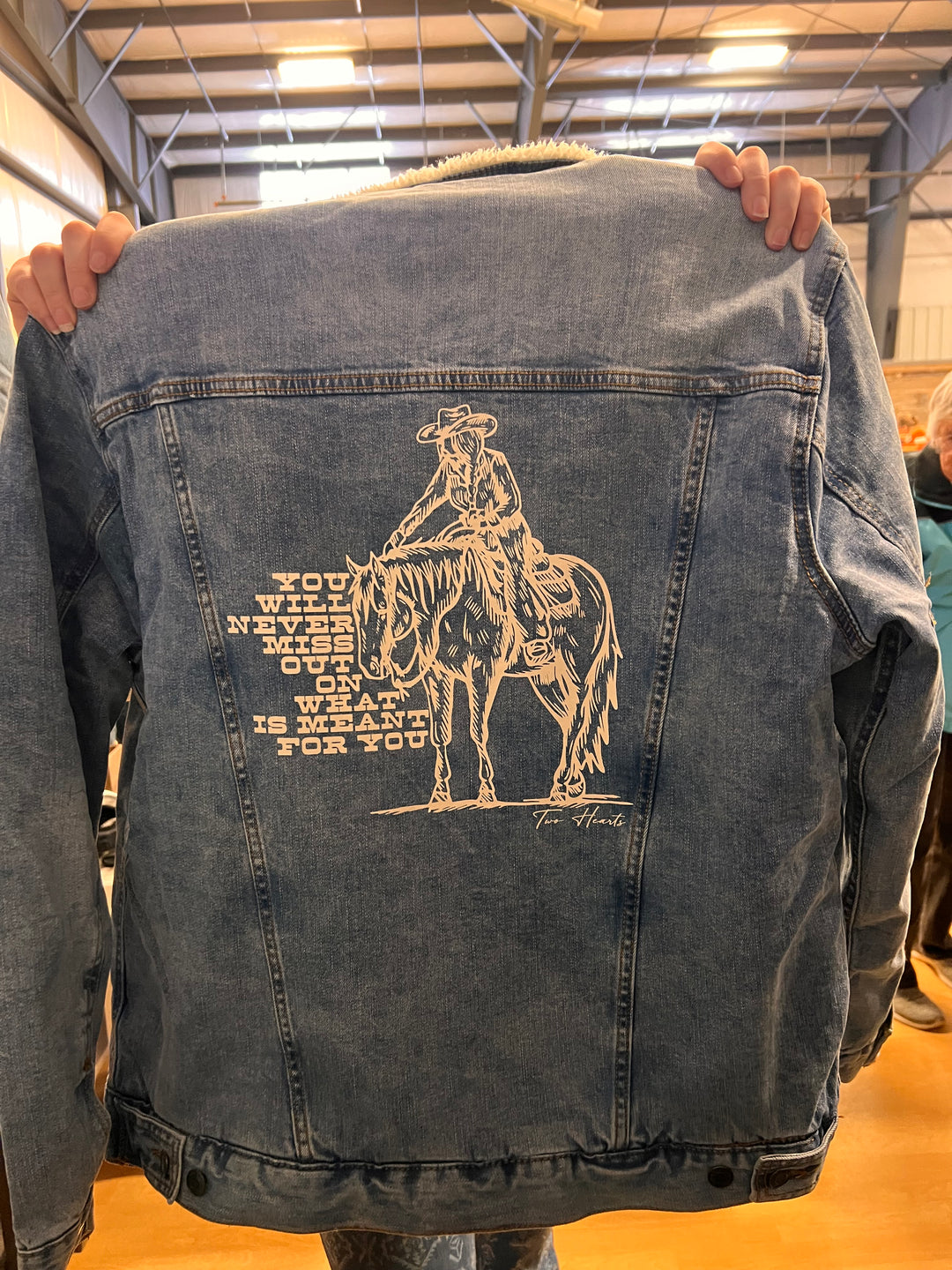 Person holding a denim jacket with a graphic design on it.