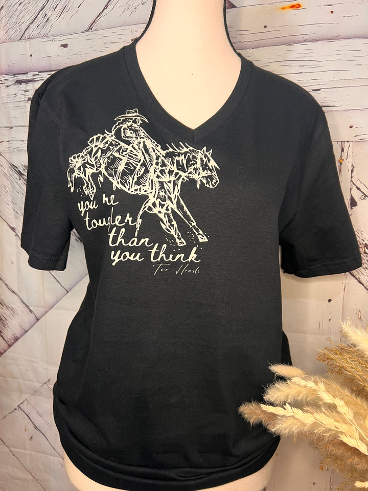 A black V-neck tee with a graphic of a cowgirl riding a bucking horse and text, paired with blue jeans and a light-colored jacket.