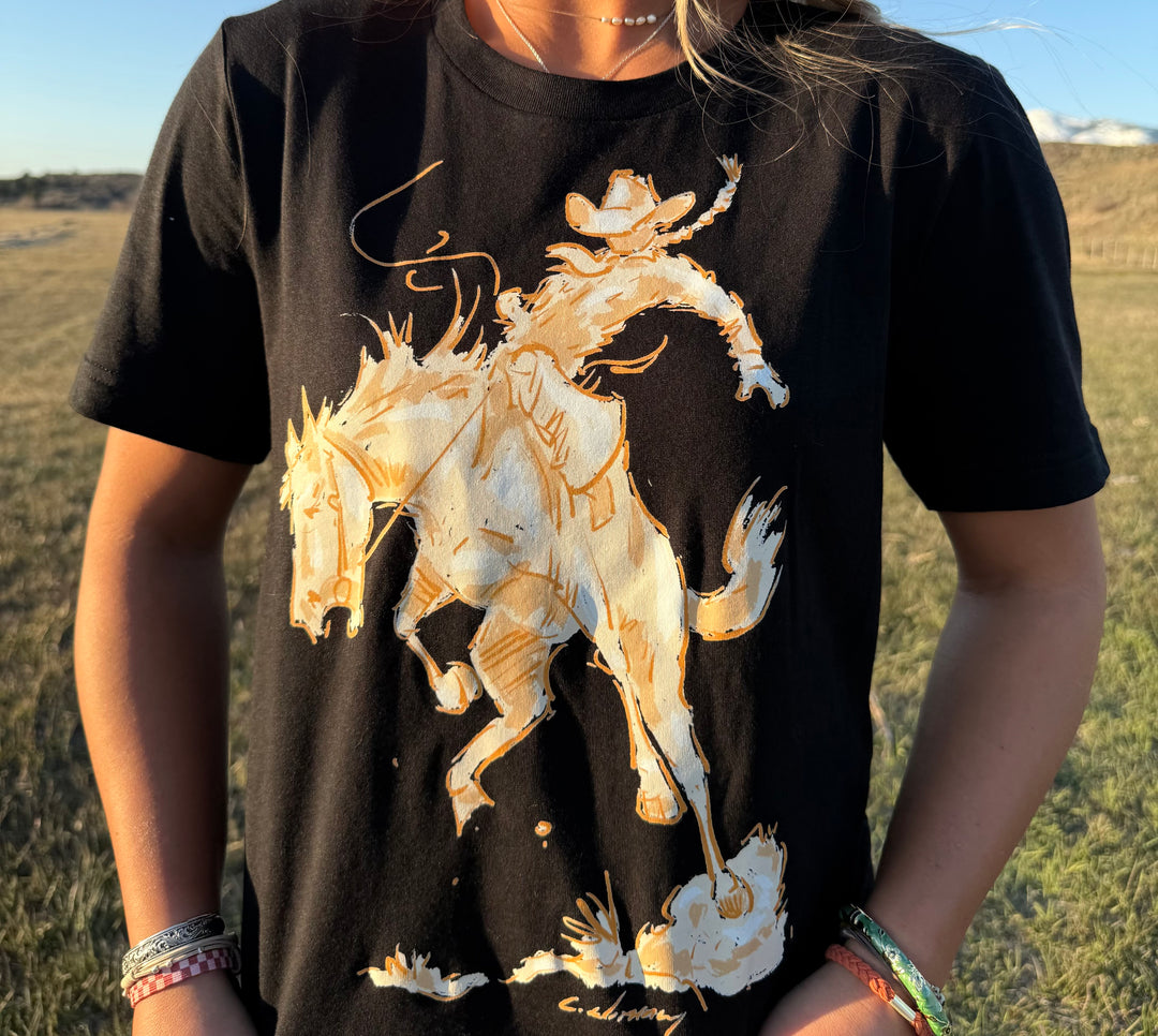 A person wearing a black t-shirt with a white and tan silhouette graphic of a cowgirl riding a bronc horse.