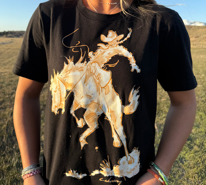 A person wearing a black t-shirt with a white and tan silhouette graphic of a cowgirl riding a bronc horse.