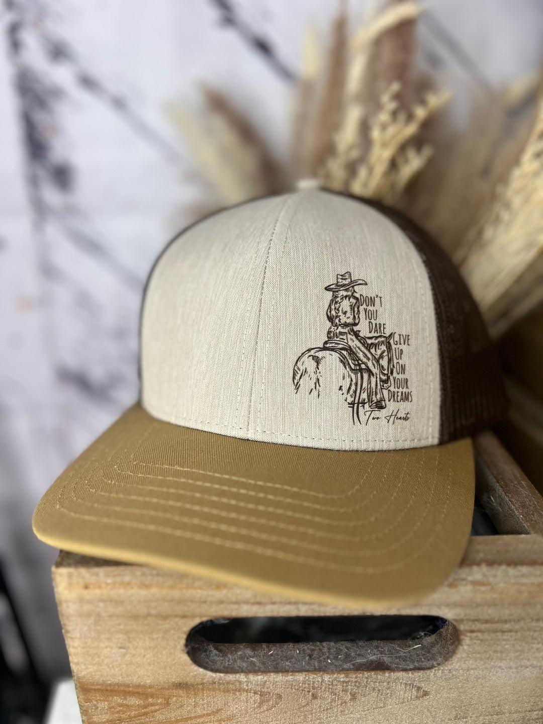 A navy and beige ballcap with a cowgirl riding a horse design, and a patterned brim, placed on a wooden surface.