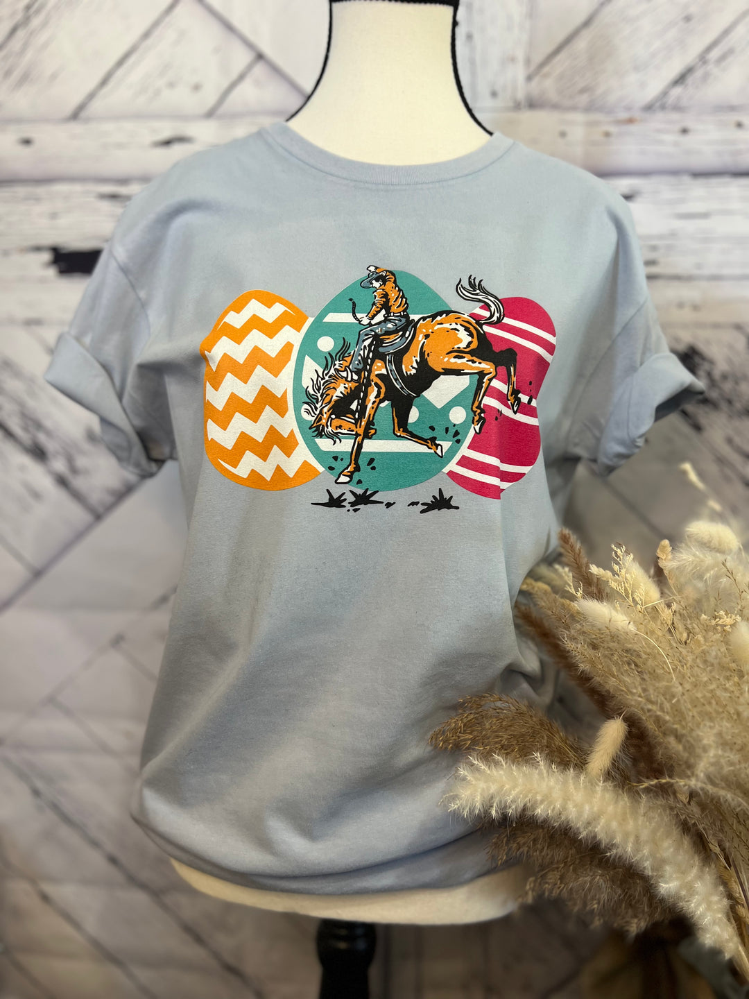 A light blue t-shirt with a graphic print of a bucking horse and Easter eggs on the front.