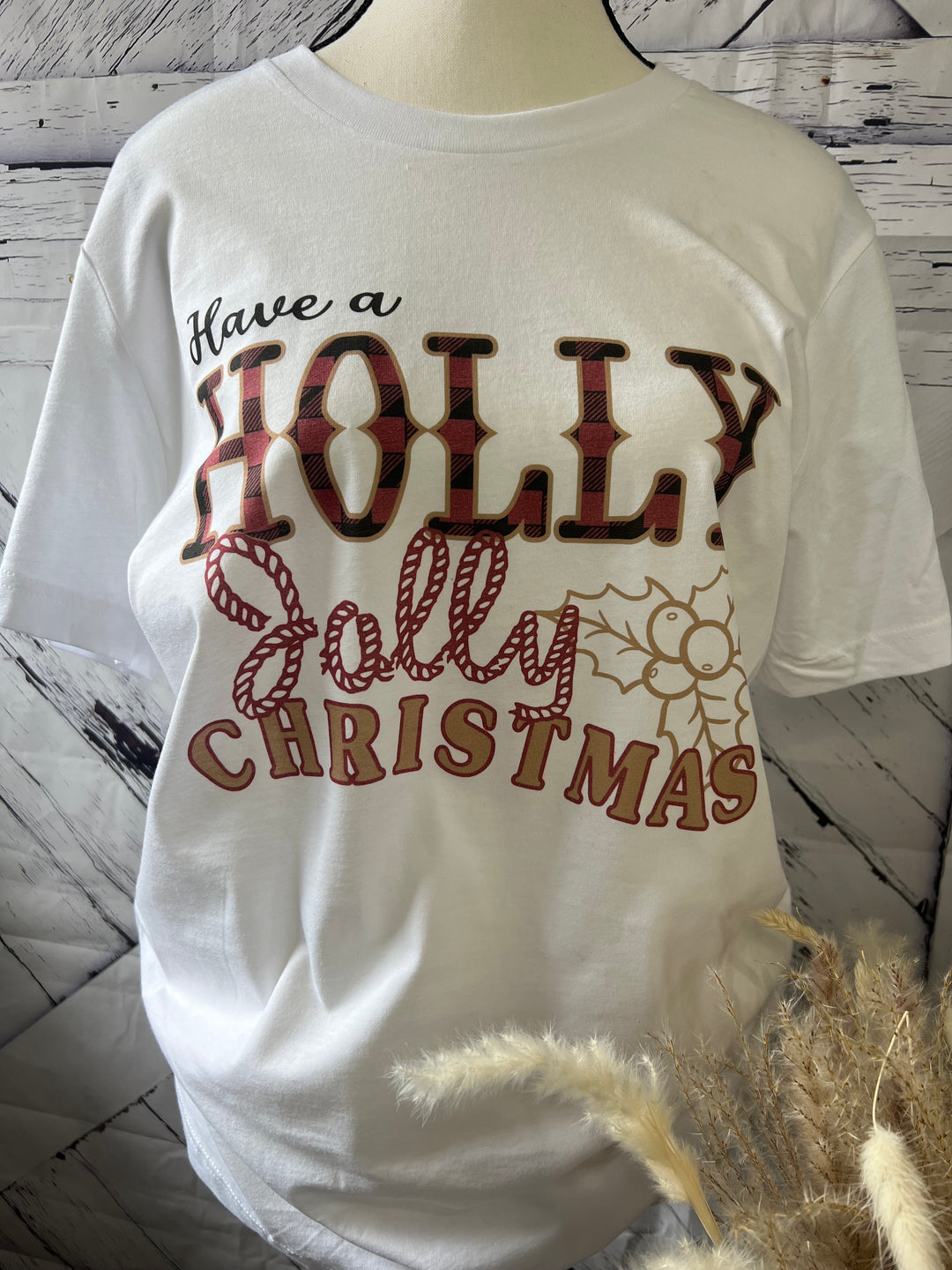 White crew neck t-shirt with 'Holly Jolly Christmas' text and holly pattern graphics.