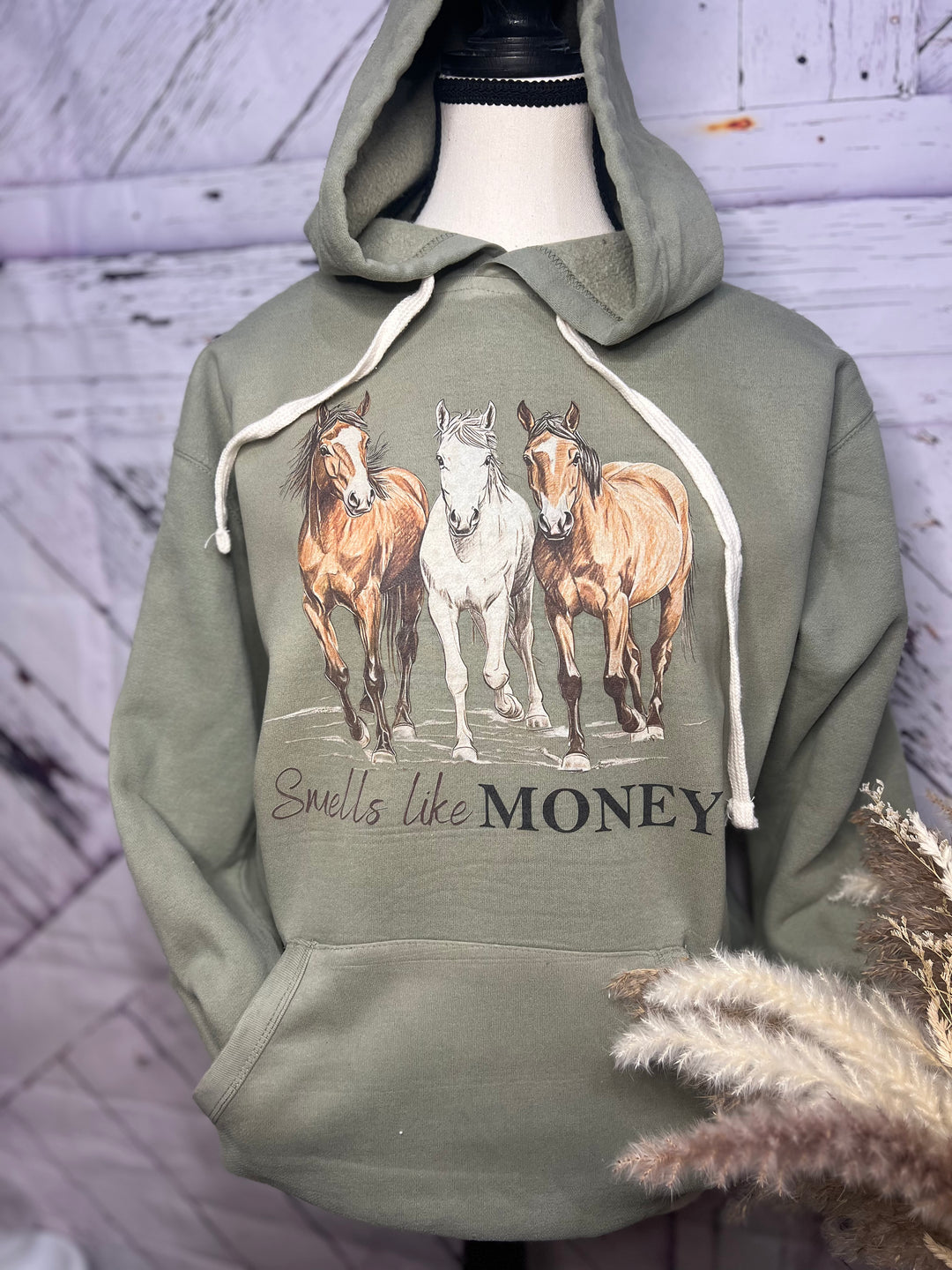 A green hoodie with a graphic of three horses and the phrase 'Smells like MONEY' on the front.