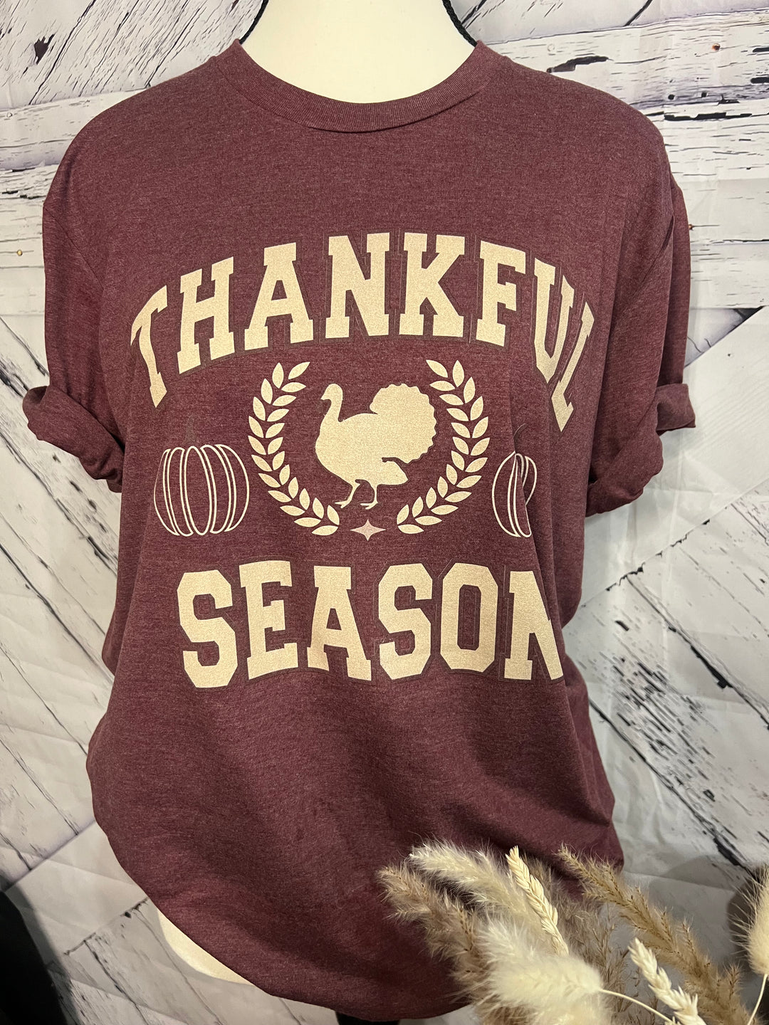A maroon t-shirt with 'THANKFUL SEASON' text and a graphic of a roasted turkey in the center, displayed on a mannequin.