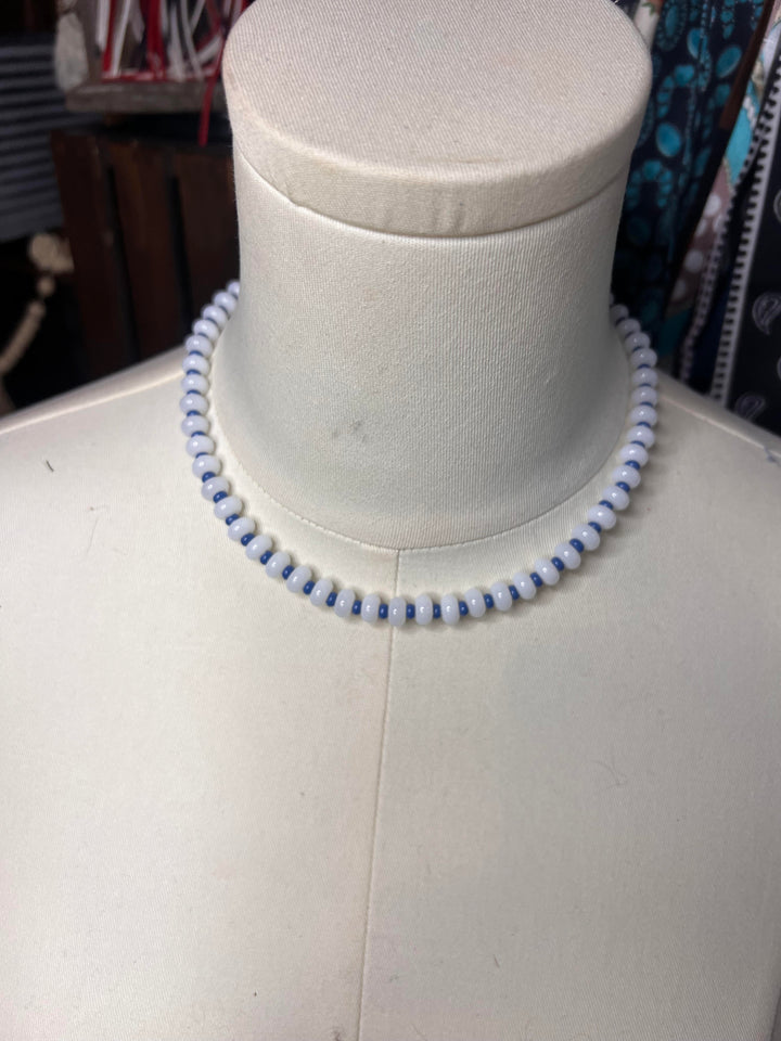 A beaded necklace with alternating light blue and white round beads, displayed on a white fabric mannequin bust.