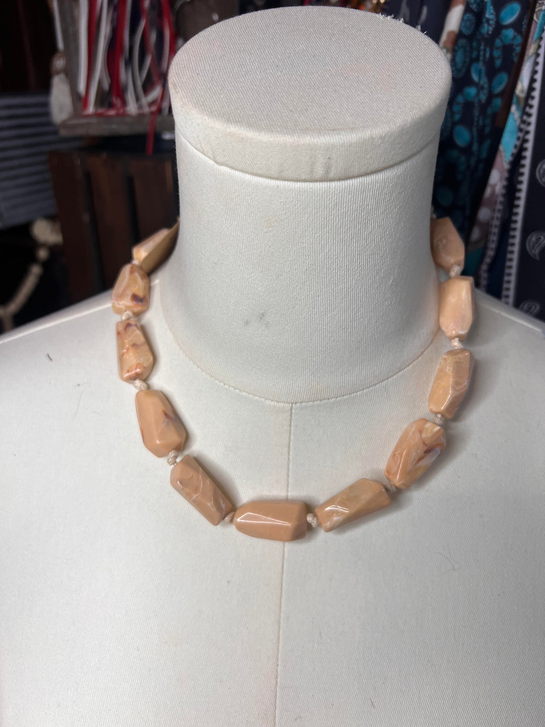 A chunky beaded necklace made of irregular, polished tan stone beads, displayed on a white fabric mannequin bust.