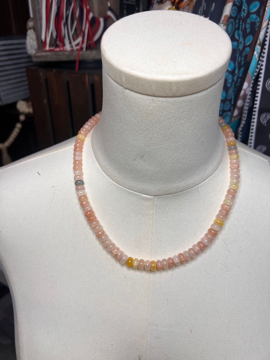 A beaded necklace made of small translucent peach-pink and yellow beads, displayed on a white mannequin bust.