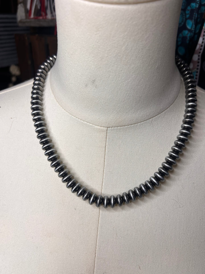 A black coiled spring necklace displayed on a white fabric mannequin bust.