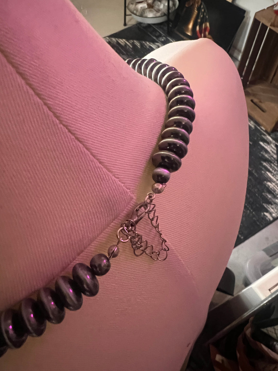 A close-up of a dark purple beaded necklace draped over a pink mannequin torso, with a silver-toned heart-shaped charm and chain extender visible.