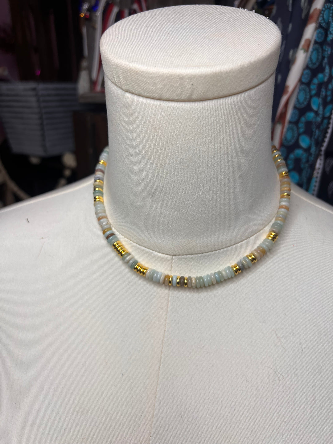 A beaded stretch bracelet displayed on a white mannequin bust. The bracelet features light blue-gray round beads separated by small metallic gold spacer beads.