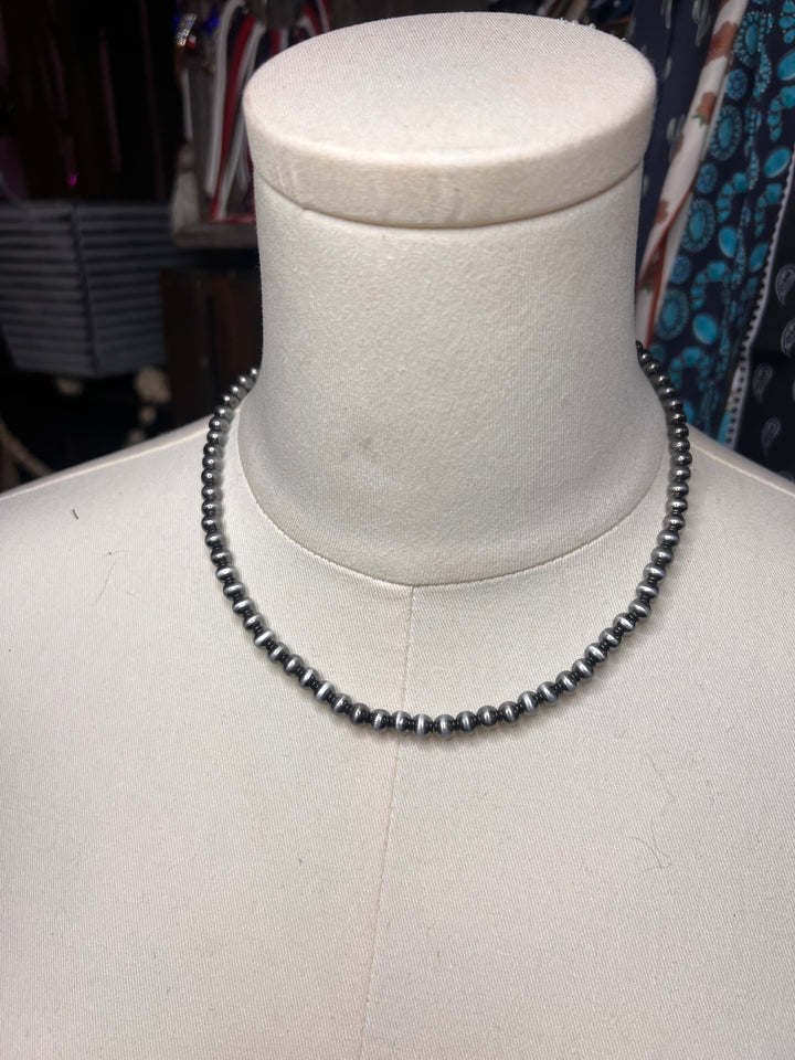 A dark gray beaded necklace displayed on a white mannequin bust, photographed indoors with a cluttered background.