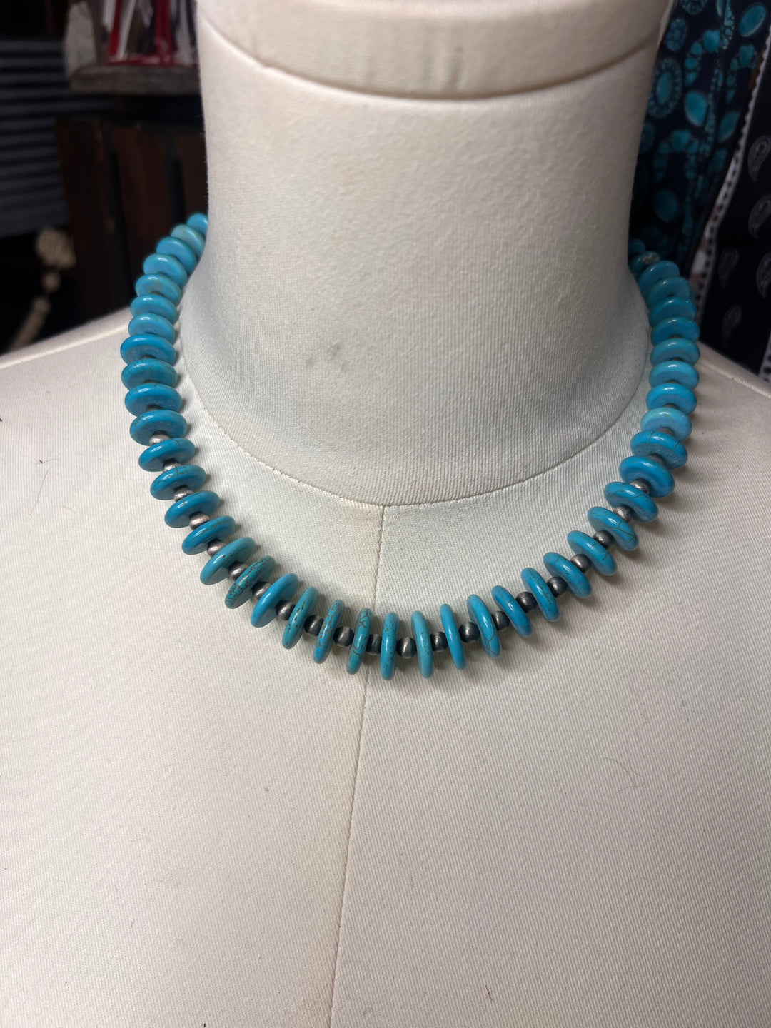 A turquoise blue beaded necklace displayed on a white fabric-covered jewelry mannequin stand against a white background.