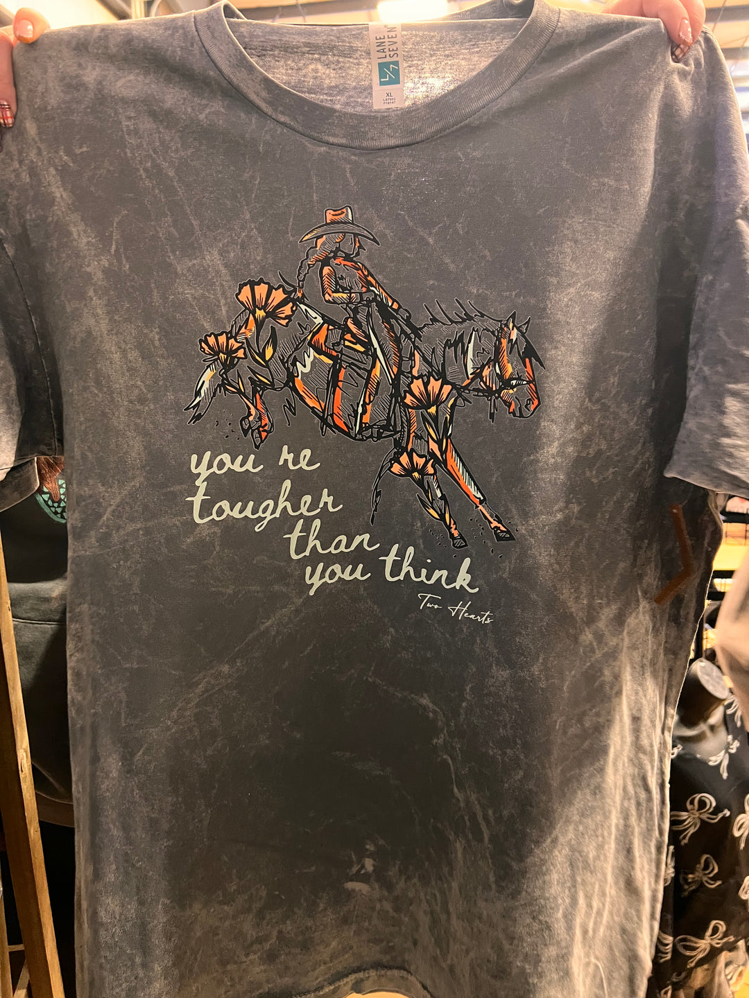 Gray t-shirt with a graphic design and text held by a person.